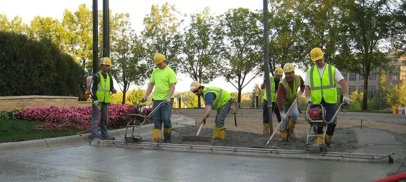 Construction crew in high-visibility safety vests using concrete screeds to level and finish large concrete slab pour