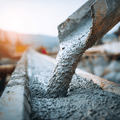 Fresh concrete pouring from a chute into a wooden form at a construction site, with a blurred background of workers and equipment.