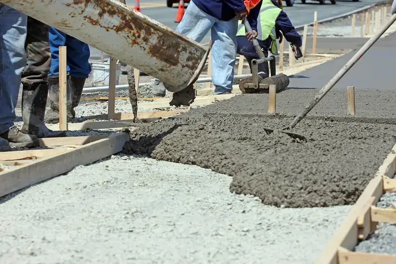 A sidewalk being poured into a wood frame from a chute