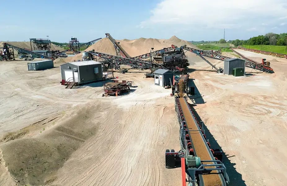 Aerial view of sand and gravel processing facility with multiple conveyor belt systems, sorting equipment, and aggregate stockpiles for concrete production
